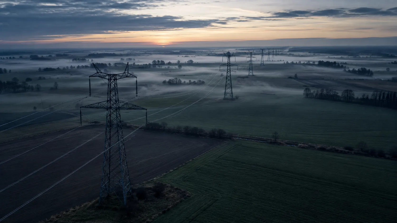 Transmission lines crossing misty farmland at dawn